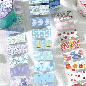 Puede incluir: Una colección de cintas adhesivas washi y pegatinas decorativas con diseños florales e inspirados en la naturaleza. Las pegatinas tienen varias formas y tamaños, con una variedad de colores como el azul, el rosa y el morado.
