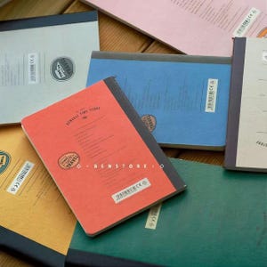 Puede incluir: Una colecci&oacute;n de cuadernos coloridos con lomos negros. Los cuadernos tienen una est&eacute;tica vintage, con las palabras "TIME TRAVEL" y "Benseli Time Store" impresas en las portadas. Los cuadernos son de varios colores, incluyendo rojo, azul, verde y amarillo.