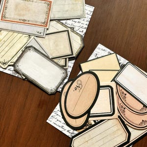 May include: A collection of rectangular and oval paper labels featuring vintage-style borders, decorative flourishes, and lines for writing. The labels are printed in shades of cream, beige, and black, with some displaying the abbreviation No.