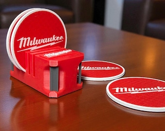 May include: A set of red and white coasters with the "Milwaukee" logo, displayed in a red holder. The coasters are round with a textured surface. The holder is red with black accents. Several coasters are stacked, with a few loose.