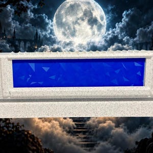 May include: A rectangular, light gray speckled stone-like display stand featuring a horizontal, recessed center panel with a vibrant blue, geometric, triangular pattern. The structure has a solid, textured base and a flat top edge.