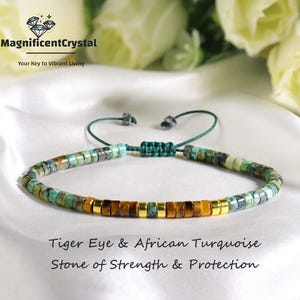以下が含まれることがあります： タイガーアイとアフリカンターコイズの石を使ったビーズブレスレット。ブレスレットは、緑色の調節可能なコードと金色のスペーサーが付いています。画像には「Tiger Eye & African Turquoise Stone of Strength & Protection」と書かれています。