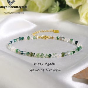 May include: A delicate bracelet featuring small, round moss agate beads in shades of green and white. The bracelet has a gold-colored chain and clasp. The text "Moss Agate Stone of Growth" is displayed below the bracelet.