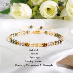 Könnte beinhalten: Ein Armband mit Citrin-, Pyrit-, Tigerauge- und Rauchquarz-Perlen. Es hat ein verstellbares, goldfarbenes Band. Der Text auf dem Bild lautet "Steine des Wohlstands & der Stärke".