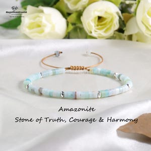 May include: An Amazonite bracelet with a light blue and silver bead design. The bracelet is on a tan cord with a sliding knot closure. The text "Amazonite, Stone of Truth, Courage & Harmony" is below the bracelet.