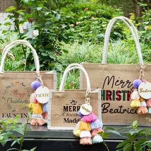 May include: Three burlap tote bags with white handles and festive Christmas designs. Each bag features a colorful tassel and a personalized wooden tag. The bags have the words "Merry Christmas" and names printed on them.