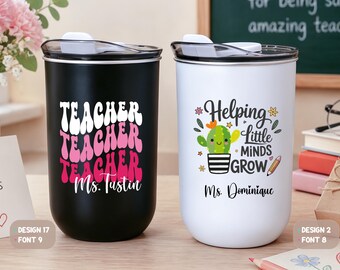 May include: A black tumbler with the text "TEACHER" repeated in white and pink wavy letters above "Ms. Tustin" and a white tumbler with a cactus graphic, the text "Helping Little MINDS GROW", and "Ms. Dominique" in black, both with clear lids.
