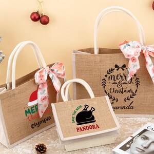 May include: Three burlap tote bags with white handles and floral bows. The bags feature Christmas-themed text and graphics, including "Merry Christmas" and a Santa hat. A small bag displays a turkey graphic and the text "Save the Neck".