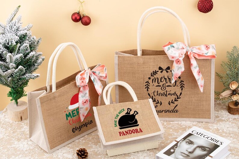 May include: Three burlap tote bags with white handles and floral bows. The bags feature Christmas-themed text and graphics, including "Merry Christmas" and a Santa hat. A small bag displays a turkey graphic and the text "Save the Neck".