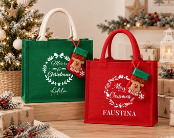 May include: A green and a red jute tote bag, each featuring white text that reads Merry Christmas and a personalized name, Adela or Faustina. Each bag includes a small hanging stocking ornament with a reindeer face and a glittery green cuff.