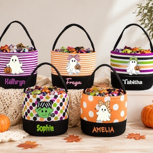May include: Five cylindrical fabric baskets with black handles and black bases, each personalized with names Kathryn, Freya, Tabitha, Sophia, and Amelia. The baskets feature colorful patterns including stripes and polka dots, decorated with ghost and monster graphics.
