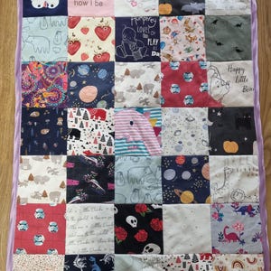 May include: A rectangular patchwork quilt featuring a variety of fabric squares with diverse prints, including a Stormtrooper, space themes, animals, and text. The quilt is bordered by a solid light purple satin binding on all four sides.