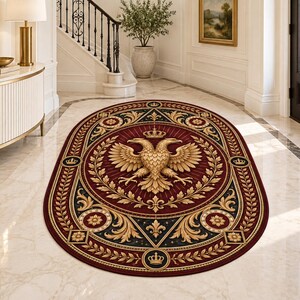 Puede incluir: Una alfombra ovalada con un centro rojo intenso y un emblema dorado de águila bicéfala coronado por una corona. El borde oscuro presenta patrones de hojas de laurel doradas, motivos de flor de lis e iconos de pequeñas coronas sobre el suelo.