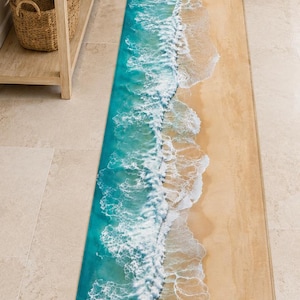 May include: A long, rectangular runner rug featuring a high-resolution photographic print of a sandy beach shoreline. The design displays a gradient of tan sand transitioning into turquoise ocean water with white, foamy waves crashing along the edge.