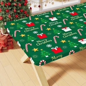 May include: A rectangular green tablecloth featuring a repeating pattern of Christmas trees, red and white gift boxes, candy canes, yellow stars, white snowflakes, and the text Merry Christmas printed in a gold script font.