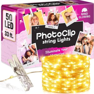 May include: A box of 50 LED PhotoClip string lights measuring 33 ft. The packaging is bright pink with images of people using the clips to hang photos. A single clear plastic clip is shown next to a coiled strand of glowing warm yellow lights.