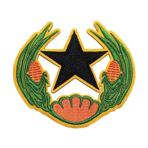 Puede incluir: Una estrella negra de cinco puntas rodeada de una corona de hojas verdes y maíz naranja. La corona está delineada en amarillo.