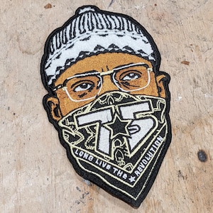 May include: Black and white embroidered patch featuring a cartoon face wearing a white knitted hat, glasses, and a bandana with the text "Long Live The Revolution" and the number "75" in white.