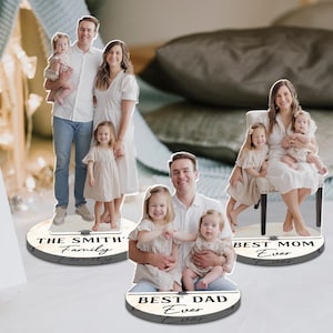 May include: Family photo cutouts on circular bases. One says "The Smith's Family", another says "Best Dad Ever", and the third says "Best Mom Ever". The cutouts feature family portraits with a light wood grain design.