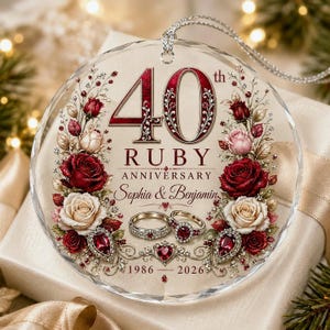 May include: A round, clear glass ornament featuring the text 40th RUBY ANNIVERSARY, Sophia & Benjamin, and 1986-2026. The design includes red and white roses, two wedding rings, and ruby-coloured gemstone accents, suspended by a silver cord.
