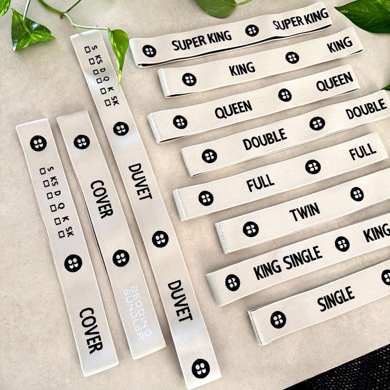 May include: White fabric bed size labels with black text. Labels include "SUPER KING", "KING", "QUEEN", "DOUBLE", "FULL", "TWIN", "KING SINGLE", and "SINGLE". Each label has a button graphic.
