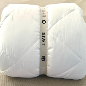 May include: A rolled-up white duvet with a diamond-stitched pattern. The duvet is secured with a light gray band that reads "DUVET" in black text. The band also features two button graphics.