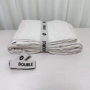 May include: A folded beige linen duvet cover with a white label that says "DOUBLE" and a white elastic band with the same text.