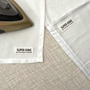 May include: Two white fabric labels with black text that reads "SUPER KING BOTTOM RIGHT CORNER" on a white fabric background.