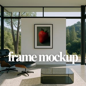 May include: A framed print of a ripe strawberry with green leaves hangs on a white wall. The room features a black leather chair and ottoman, a glass coffee table, and large windows overlooking a green landscape. The text "frame mockup" is displayed.
