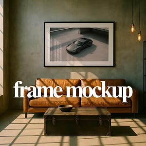 May include: A living room scene featuring a brown leather sofa, a dark wooden trunk used as a coffee table, and a framed picture of a car. The words "frame mockup" are displayed in white text. The room has large windows and a minimalist design.