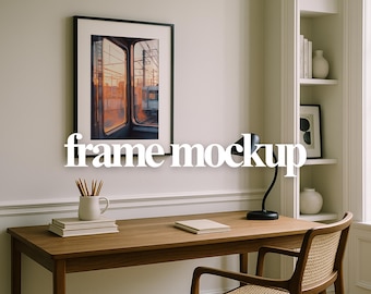 May include: A framed art print depicting a train window scene at sunset, with orange and yellow tones. The black framed print hangs above a wooden desk with a black desk lamp, books, and pencils in a white mug. The text "frame mockup" is overlaid on the image.