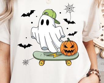 May include: White t-shirt featuring a cartoon ghost wearing a green cap, riding a skateboard with a pumpkin and lightning bolt design. Black bats and spiderwebs are also featured in the design. Halloween themed apparel.