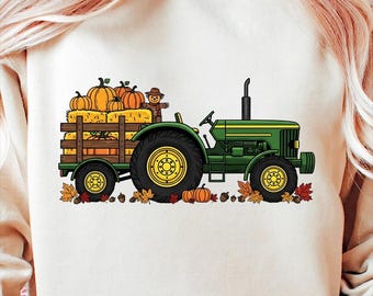 May include: A cream-colored sweatshirt featuring a green tractor pulling a wooden wagon filled with pumpkins and hay. A scarecrow is seated in the wagon. Fall leaves and pumpkins are scattered around the tractor's wheels, creating a seasonal theme.