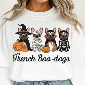 May include: White sweatshirt featuring four French Bulldogs dressed in Halloween costumes. One dog is a witch, another a mummy, a third a vampire, and the last a skeleton. The words "French Boo-dogs" are printed below the dogs.
