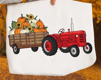 May include: A white tote bag featuring a red tractor pulling a wooden wagon filled with pumpkins and sunflowers. The pumpkins are orange, white, and green. The tractor has black tires and a silver exhaust pipe. The background is blurred.