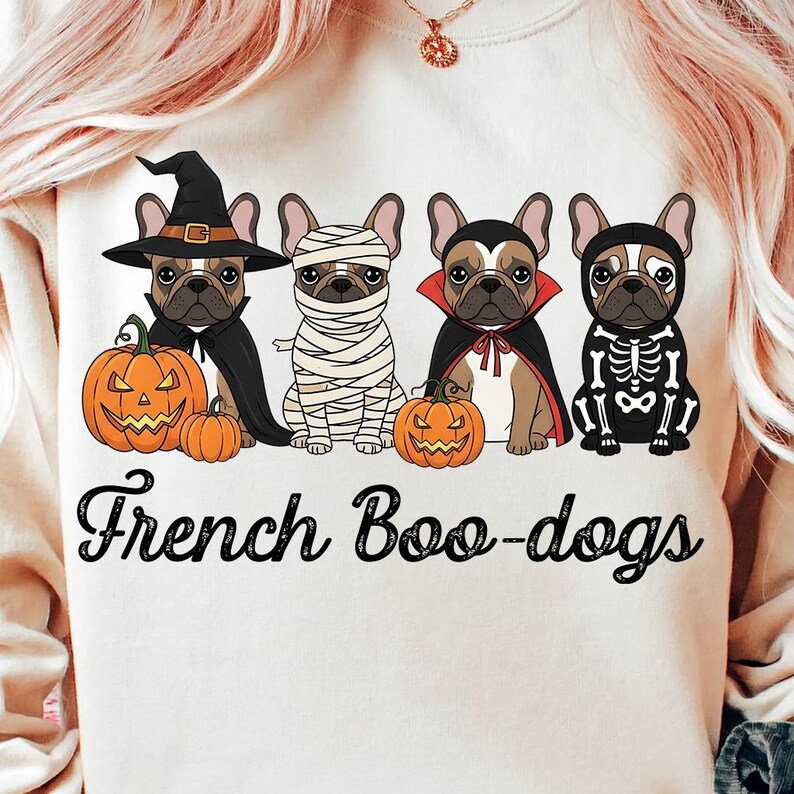 May include: A cream-colored sweatshirt featuring four French Bulldogs dressed in Halloween costumes. The dogs are wearing a witch hat, mummy bandages, a vampire cape, and a skeleton costume. The text "French Boo-dogs" is printed below the dogs.