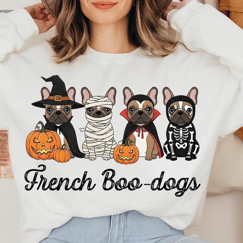 May include: White sweatshirt featuring a Halloween-themed graphic. The design includes four French Bulldogs dressed in costumes, with pumpkins and the text "French Boo-dogs" in black script.