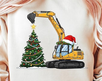 Puede incluir: Excavadora amarilla con gorro de Papá Noel y luces navideñas, junto a un árbol de Navidad decorado con una estrella. El brazo de la excavadora está posicionado para colocar la estrella en el árbol. El diseño está en una sudadera crema.
