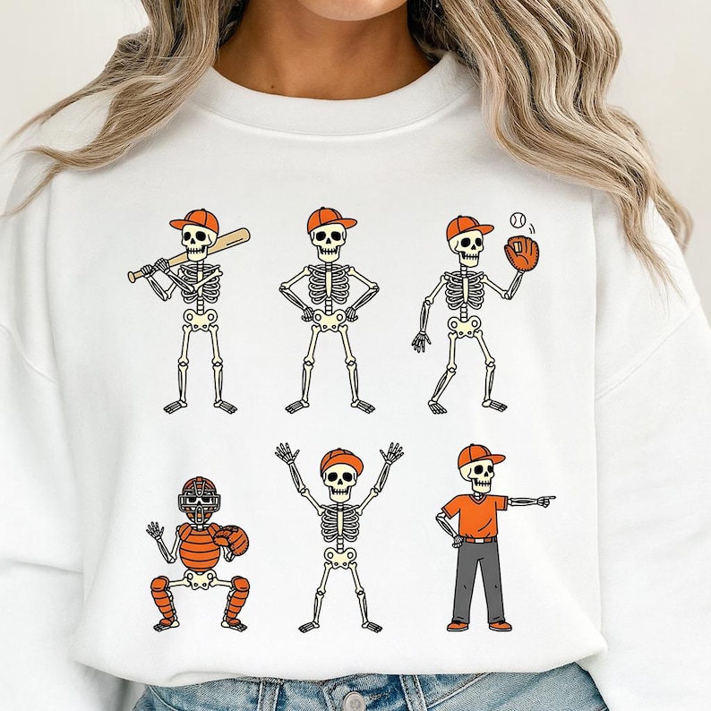 May include: White sweatshirt featuring six skeleton baseball players in orange caps and uniforms. The skeletons are in various baseball positions, including batting, pitching, and catching. A fun, sporty design for Halloween or baseball fans.