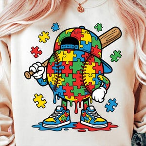 May include: Cream-colored sweatshirt featuring a baseball character made of puzzle pieces in red, yellow, green, and blue. The character wears a baseball cap and sneakers, holding a bat. Additional puzzle pieces are scattered around.