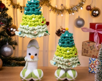 May include: Crocheted Christmas tree ornaments and a snowman. The trees are green and yellow with decorative accents. The snowman is white with a carrot nose and a green and white striped base. Festive holiday decor.