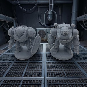 May include: Two unpainted grey resin miniature robot figures standing on circular bases. The left robot features a smooth helmet and a rectangular shield on its arm. The right robot has a multi-lens sensor array on its chest and articulated claw hands.