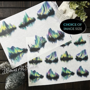 May include: Sheets of watercolor-style decals featuring a mountain and aurora borealis design. The decals showcase vibrant colors of green, yellow, and purple against a black silhouette of trees. The text "Choice of Image Size" is visible.