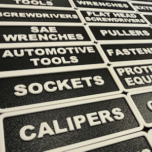 May include: Black and white tool labels with raised white lettering. Labels include "Automotive Tools", "Sockets", "Calipers", "Protective Equipment", "Grinder", and more. Useful for workshop organisation.