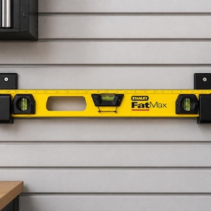 May include: A yellow Stanley FatMax spirit level mounted horizontally on a wall. The tool features black end caps, three green liquid-filled vials for leveling, and a printed ruler along the top edge. The brand name FatMax is printed in black.