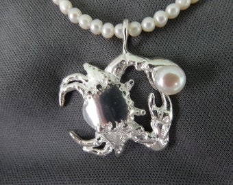 Crab holding pearl pendant