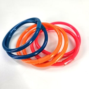 May include: A collection of colorful bracelets in shades of blue, orange, and pink. The bracelets are made of a smooth, glossy material and are arranged in a slightly overlapping pattern. The bracelets are a fun accessory.