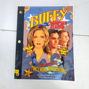 May include: A Buffy the Vampire Slayer script book titled "Once More, With Feeling." The cover features illustrations of the main characters and the show's title in a stylized font. The book includes a full-color photo insert and sheet music.