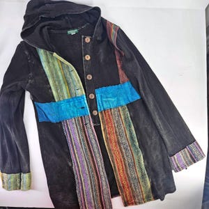 Puede incluir: Chaqueta negra con capucha y detalles de patchwork coloridos. La chaqueta tiene una parte delantera abotonada, una capucha y mangas largas. El patchwork incluye rayas azules, verdes, rojas y moradas. Los puños y el dobladillo también están adornados con tela estampada.