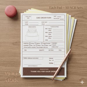 Puede incluir: Una pila de formularios de pedido de pasteles con un bolígrafo y un macaron rosa sobre una superficie de madera. Los formularios tienen secciones para los detalles del cliente, bocetos de diseño y detalles de sabor. El texto "Cake Order Form" es visible.
